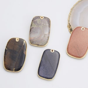 Può includere: Quattro ciondoli rettangolari in pietra con cornici in metallo dorato e un anello per l'appeso. Le pietre sono in tonalità di marrone, rosa, blu e grigio.