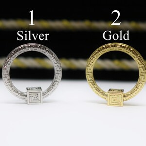 May include: Two silver and gold rings with a square design in the center. The rings have a Greek key pattern around the outside.