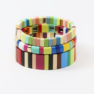 May include: Three colorful bracelets stacked on top of each other. The bracelets are made of small, square beads in a variety of colors, including red, orange, yellow, green, blue, and purple.