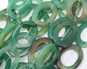 May include: A close-up of a pile of green agate oval beads with a hole in the centre. The beads are smooth and polished, and have a natural, organic look.