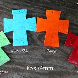 May include: Four wooden crosses painted in different colours: light blue, orange, light green, and red. Each cross measures 8.5 by 7.4 centimetres. The crosses are arranged in a row on a wooden surface.