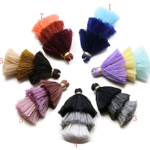 Può includere: Assortimento di dieci frange multi-colorate con due strati di nappe. Le frange sono in tonalità beige, marrone, nero, viola, rosa, blu, giallo e arancio.