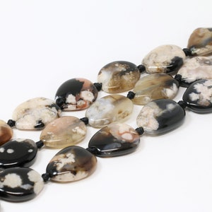 May include: A strand of black and white agate gemstone beads with a natural, organic pattern. The beads are oval shaped and strung on a black cord.