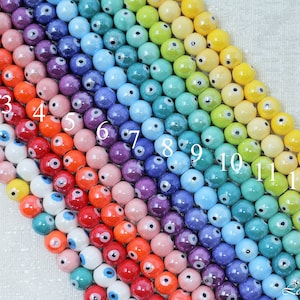 May include: A rainbow assortment of 13 ceramic beads with an evil eye design. The beads are round and have a glossy finish. The beads are numbered 1 through 13.
