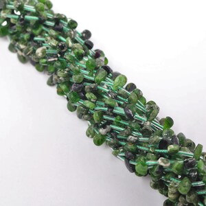 May include: A strand of green and black gemstone beads, with a faceted, irregular shape. The beads are strung on a thin wire.