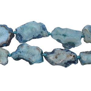 Pode incluir: Um fio de contas de ágata azul com formas irregulares e textura natural e áspera. As contas são enfiadas com fio turquesa.
