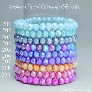 Könnte beinhalten: Ein Stapel von acht dehnbaren Armbändern aus 8 mm Kristallperlen. Die Armbänder sind in Blautönen, Lila, Rosa und Orange. Die Armbänder sind von 201 bis 209 nummeriert.