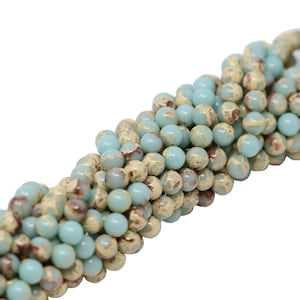 May include: A strand of light blue and brown marbled round beads. The beads are approximately 6mm in diameter.