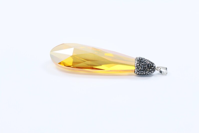 May include: A teardrop-shaped pendant with a faceted, yellow crystal and a silver bail adorned with black rhinestones.