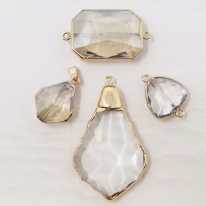 Könnte beinhalten: Vier klare Glasanhänger mit goldenen Metallakzenten. Die Anhänger haben verschiedene Formen, darunter ein Rechteck, eine Träne und zwei Diamanten.