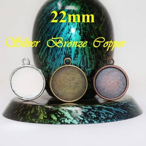 May include: Three 22mm round metal pendant blanks in silver, bronze, and copper. The blanks are on a black and green surface.