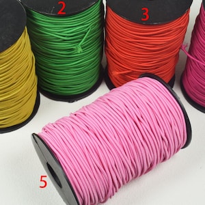 May include: Five spools of colorful cord in yellow, green, red, pink, and hot pink. Each spool is tightly wound and labeled with a number. The cords are likely used for crafting or jewelry making.