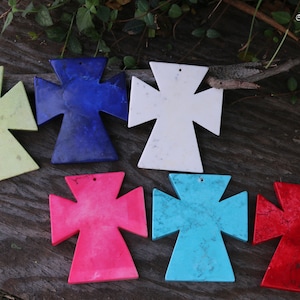 May include: Six different coloured cross-shaped pendants made of stone. The colours are green, blue, white, pink, turquoise, and red.