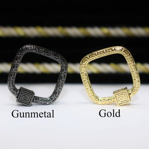 May include: Two square-shaped metal keychains with a geometric design. The keychain on the left is gunmetal and the keychain on the right is gold.