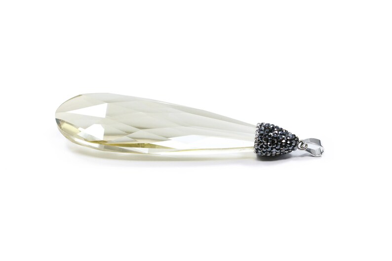 May include: A teardrop-shaped crystal pendant with a silver tone setting. The setting is covered in small black crystals.