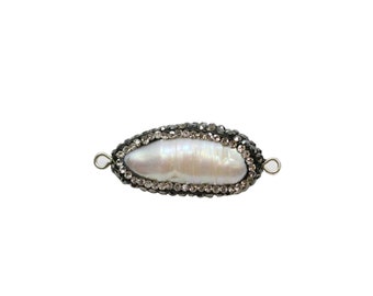 May include: A white baroque pearl with a silver setting and a border of clear rhinestones. The pearl is oval shaped and has a slight iridescent sheen.