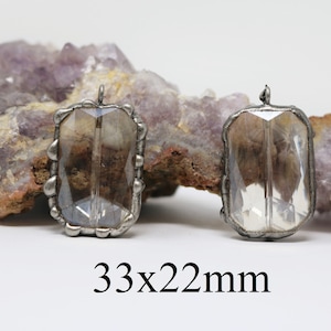 Puede incluir: Dos colgantes rectangulares de vidrio transparente con marcos de metal plateado. Los colgantes miden 33 mm por 22 mm.
