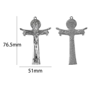 Op de afbeelding: Een zilverkleurige metalen crucifix hanger van 76,5 mm bij 51 mm. De voorzijde toont een figuur aan het kruis met een hoofd met aureool erboven en een duif aan de basis. De achterzijde bevat de tekst 'TERTIUM MILLENNIUM' met symbolen aan de uiteinden.