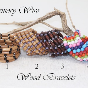 Puede incluir: Cuatro pulseras de madera con cuentas de diferentes colores. Las pulseras están hechas con alambre de memoria y están apiladas en una rama. Las pulseras están numeradas del 1 al 4. El texto "Memory Wire Wood Bracelets" está escrito debajo de las pulseras.