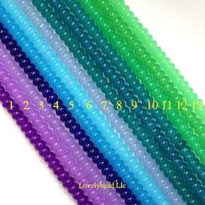 Peut inclure: Treize brins parallèles de perles rondes et lisses disposés en un dégradé de couleurs allant du violet au bleu foncé, bleu clair, sarcelle et diverses nuances de vert. Chaque brin est numéroté de 1 à 13 en jaune, avec le texte Lovelybead Llc.