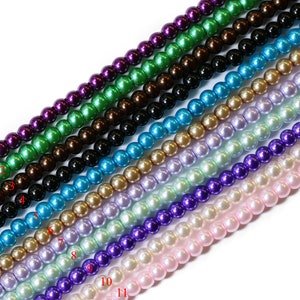 May include: A strand of 11 different colours of round, pearl-like beads. The colours are purple, green, brown, black, teal, gold, lavender, light green, purple, pink, and white.