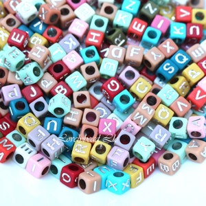 Peut inclure: Un grand tas de perles de lettres de l'alphabet colorées. Les perles sont en plastique et ont une lettre argentée de chaque côté. Les perles sont de différentes couleurs, notamment rouge, bleu, vert, jaune, rose et orange.