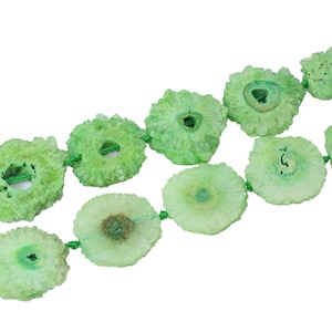 May include: A strand of green agate crystal beads, each bead is a round slice with a hole in the center, the beads are strung on a green cord.