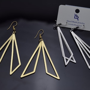 May include: Two pairs of geometric dangle earrings. One pair is gold and the other is silver. The earrings are made of metal and have a triangular shape.