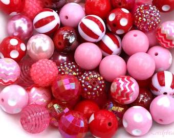 Könnte beinhalten: Eine Sammlung von rosa und roten Perlen mit verschiedenen Mustern und Texturen, darunter Punkte, Streifen, Zickzackmuster und Glitzer.