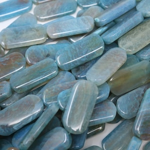 May include: A collection of smooth, light blue agate gemstone beads with a mottled pattern. The beads are oval shaped and have a polished finish.