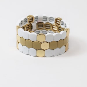 May include: A white and gold bracelet made of interlocking round beads. The bracelet is made of two rows of white beads and one row of gold beads.