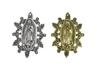 Puede incluir: Dos colgantes de metal de 50x37mm, uno en tono plateado y otro en tono dorado. Cada colgante presenta una figura central en relieve de la Virgen de Guadalupe rodeada por un marco ornamentado de hojas y volutas con una pequeña argolla.