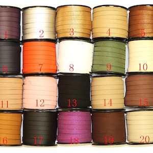 Op de afbeelding: Twintig spoelen met lederen koord in verschillende kleuren, waaronder zwart, bruin, beige, oranje en paars. Elke spoel is genummerd van 1 tot 20.
