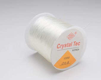 以下が含まれることがあります： 「Crystal Tec Korea」と「100M 0.8」のラベルが付いた白い伸縮性のあるコードの糸巻きです。