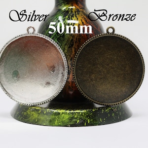 Könnte beinhalten: Zwei runde Metall-Anhänger-Rohlinge, einer silberfarben und einer bronzefarben, mit einem perlenbesetzten Rand. Beide haben einen Durchmesser von 50 mm.