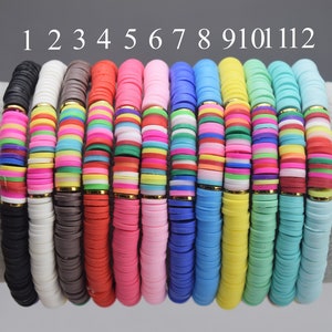 Peut inclure: Douze bracelets colorés faits de perles en céramique rondes, plates et empilées. Les bracelets sont disposés en rangée, numérotés de 1 à 12. Chaque bracelet a une couleur et un motif différents.