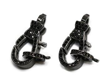 May include: Two black metal lobster clasps, encrusted with small black gemstones. The clasps are shown against a white background. These jewelry findings are designed for securing necklaces, bracelets, or other accessories.