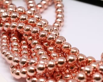 Op de afbeelding: Een streng ronde kralen in rosé-goud. De kralen zijn glad en glanzend en liggen los in een hoop.
