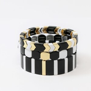May include: Three stacked bracelets with black and white geometric patterns and gold accents.