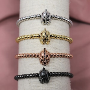May include: Four beaded bracelets with a black helmet charm. The bracelets are silver, gold, rose gold, and black.