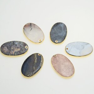 May include: Six oval-shaped agate gemstone pendants with gold-toned edges and a hole for stringing. The stones are in various shades of brown, gray, and white.