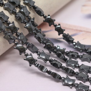 May include: A strand of black hematite beads, each bead is shaped like a turtle. The beads are strung together to form a chain.
