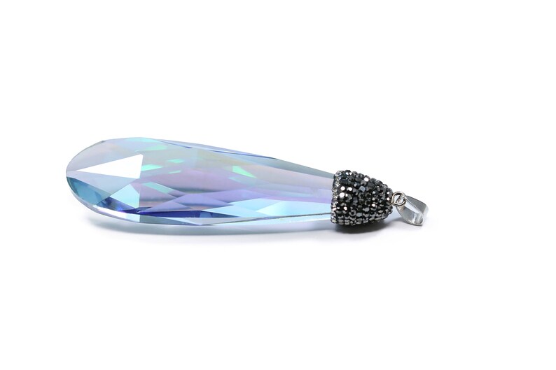 May include: A teardrop-shaped crystal pendant with a silver-tone setting and a black crystal accent. The crystal is iridescent and reflects light in shades of blue and purple.