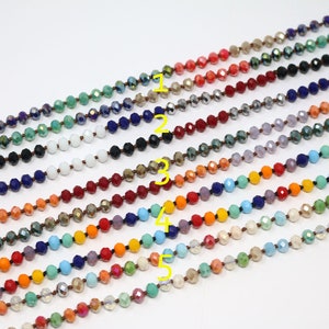 May include: A collection of 10 strands of faceted glass beads in various colors, including turquoise, orange, red, and purple. The beads are strung on a clear thread and are arranged in a fan shape.