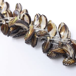 Puede incluir: Una hebra de cuentas de concha marrón y blanca con forma de hojas. Las cuentas están enhebradas en un hilo transparente.