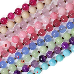May include: Rows of colorful gemstone beads in shades of red, pink, blue, green, and purple. Each bead is round and strung on a brown cord. The beads vary in size and color intensity, creating a gradient effect.