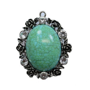 May include: A silver pendant with a turquoise cabochon stone set in a decorative frame with clear rhinestones.