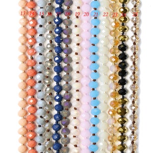 May include: A selection of 12 strands of faceted glass beads in various colors, including peach, gray, blue, white, pink, light blue, gold, and black. The beads are strung on a clear thread.