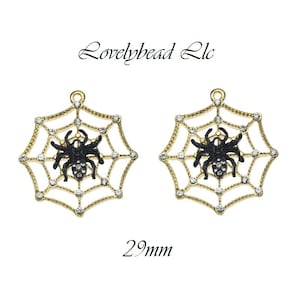 May include: Two gold-toned spiderweb charms with black spiders at the center. Each web is adorned with clear crystals. The charms are 29mm in size and have a loop at the top for hanging. The text "Lovelybead Llc" is at the top.