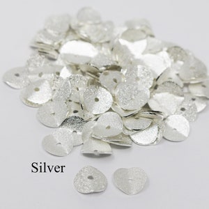 May include: A pile of silver heart-shaped metal beads with a hole in the center. The beads have a textured surface. The word "Silver" is written below the pile of beads.
